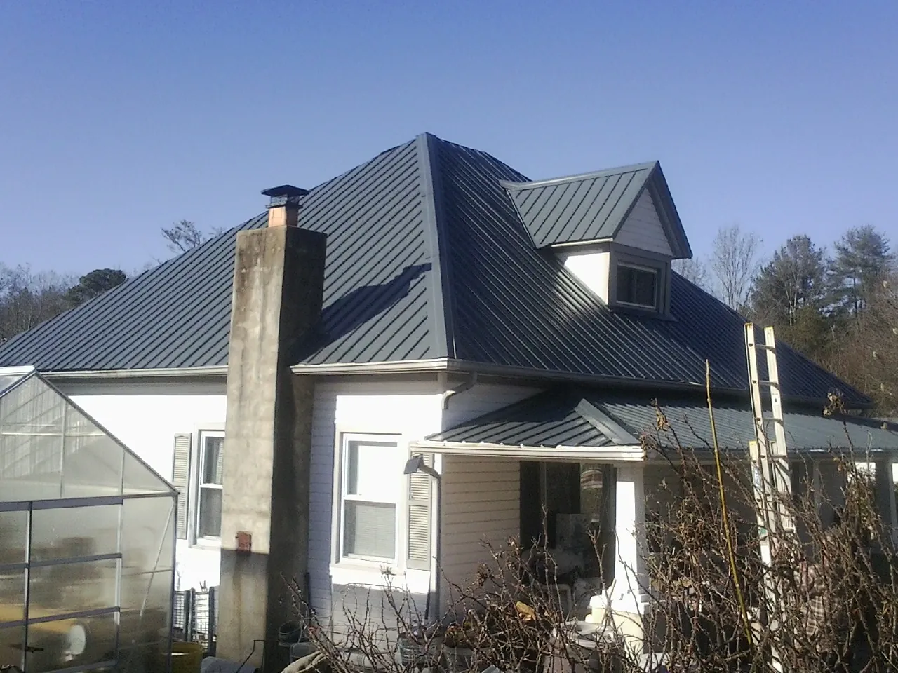 Dark blue standing seam metal roof on a white farmhouse with dormer — Slate & Tile Roof Repair by Roofing Brothers in Porterdale
