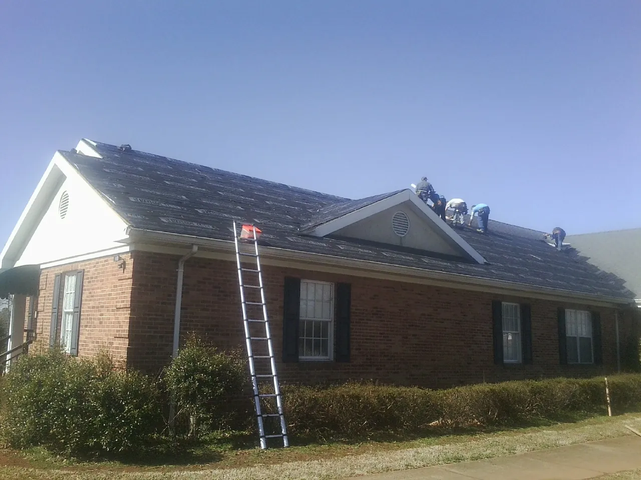 Crew tearing shingles off a brick ranch roof with a ladder set — Emergency Roof Repair work by our crew in Porterdale