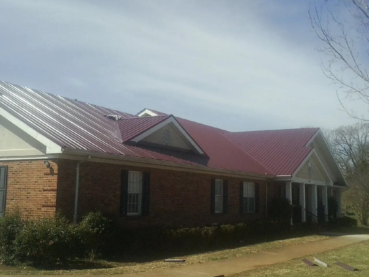 Red metal roof with gabled entries on a long brick building, from a Hail Damage Roof Repair job in Porterdale