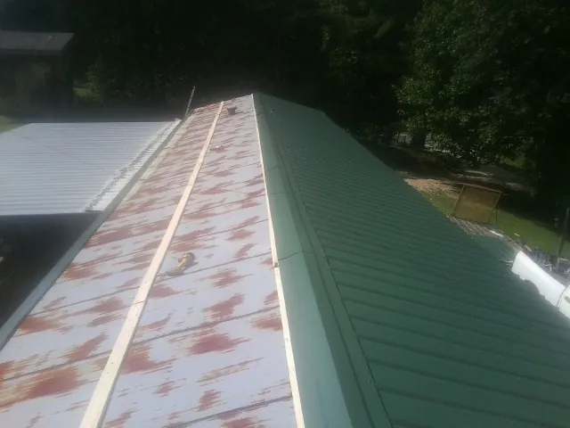 Old rusted panels beside newly installed green metal roofing — Wind Damage Roof Repair by Roofing Brothers in Porterdale