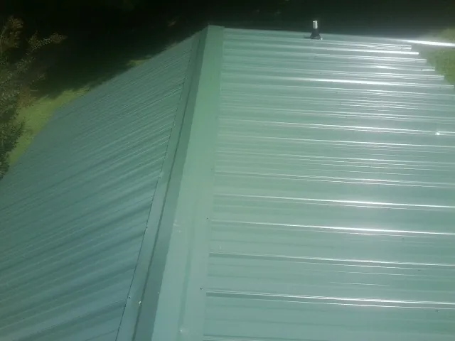 New green metal panels meeting at the ridge of a roof — Flat Roof Repair work by our crew in Porterdale
