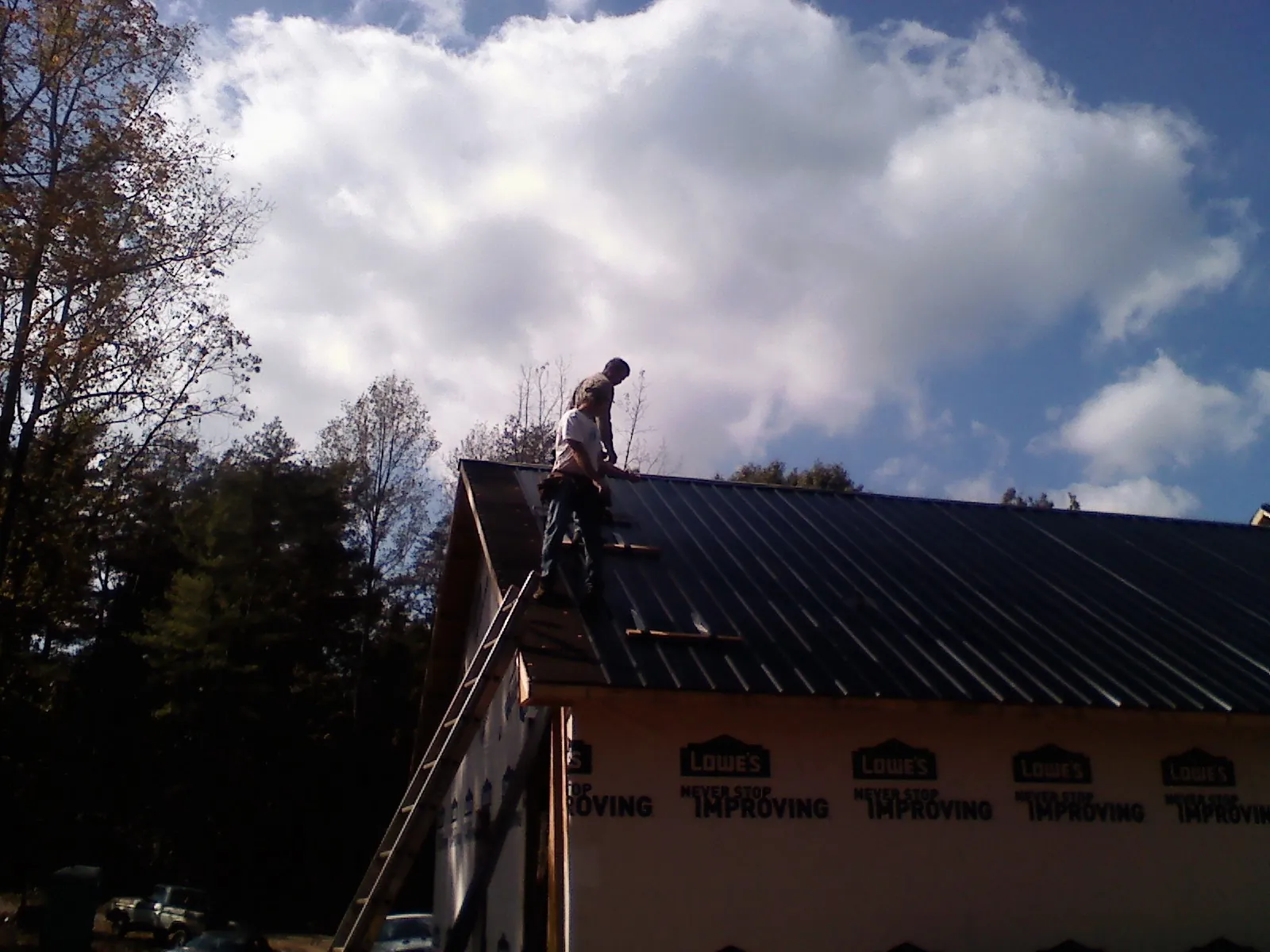 Roofer fastening dark metal panels high against a cloudy sky, from a Roof Inspection job in Porterdale