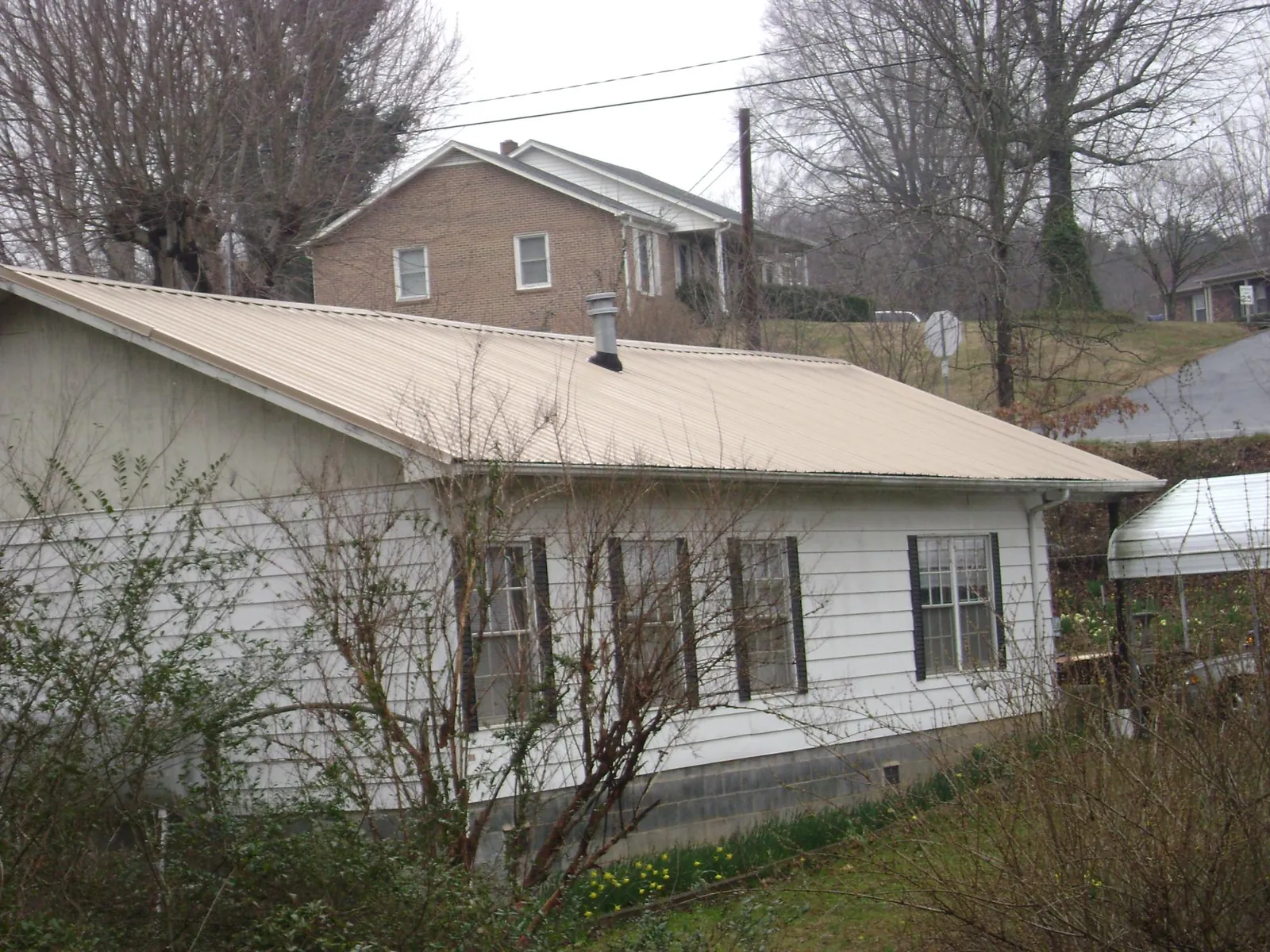 Tan metal roof on a white sided house set into a hillside — Commercial Roofing by Roofing Brothers in Porterdale