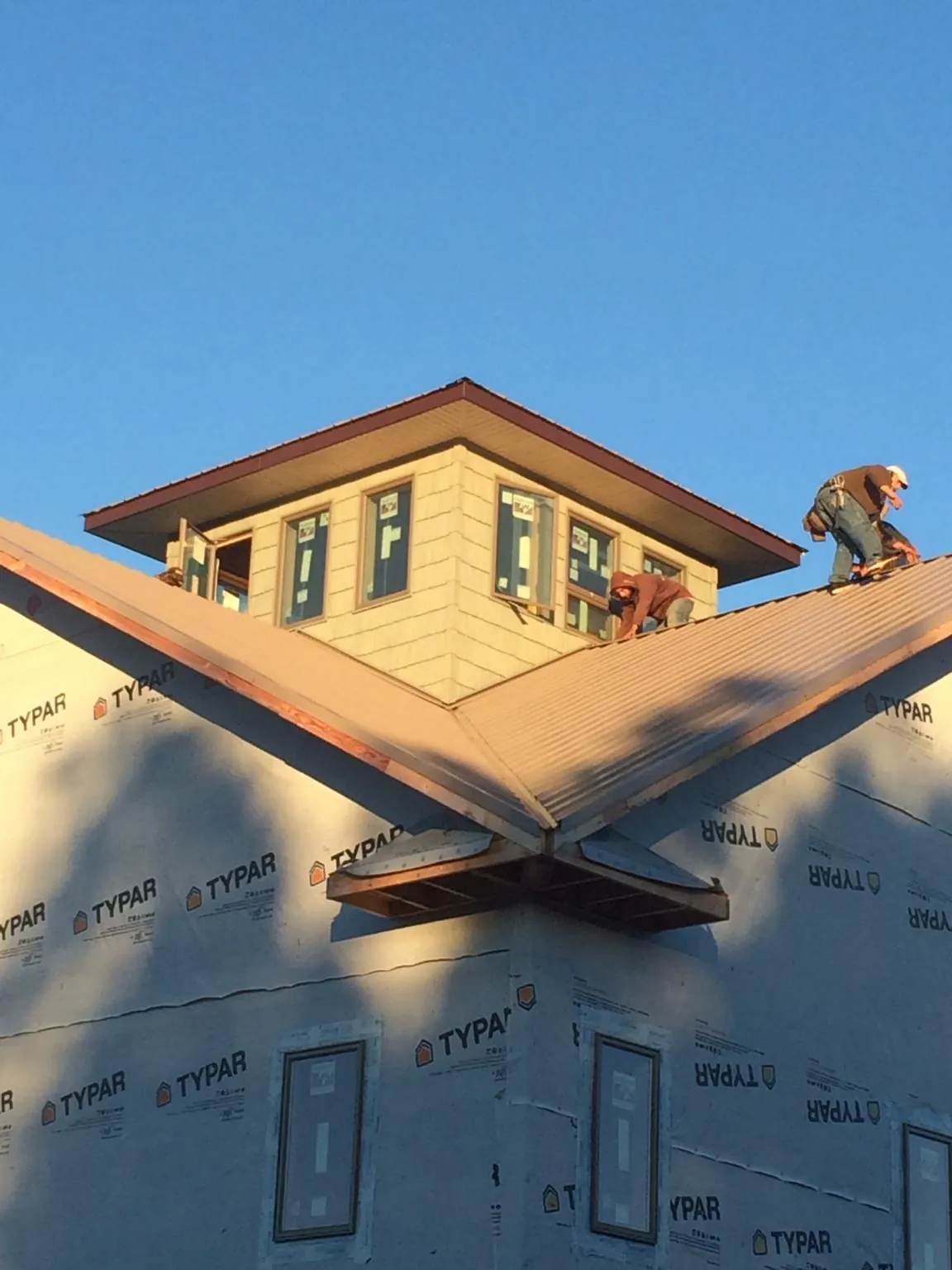 Roofers working around a rooftop cupola on a new metal roof at sunset — Roof Waterproofing in Porterdale by Roofing Brothers
